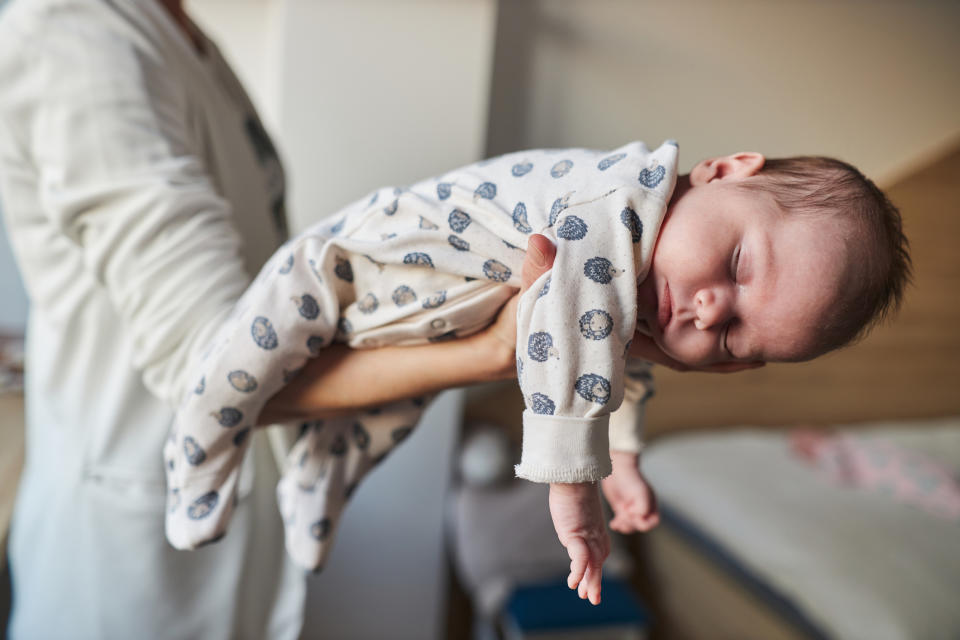 Person holding a sleeping baby in a onesie. The baby is cradled gently in their arms