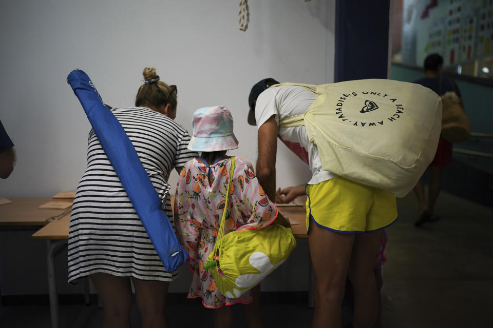 A family carrying their things for the beach prepare their ballots at a polling station in Badalona, outskirts of Barcelona, Spain, Sunday July 23, 2023. Polling began Sunday in Spain in a general election that could make the country the latest European Union member to swing to the political right.(AP Photo/Joan Mateu Parra)