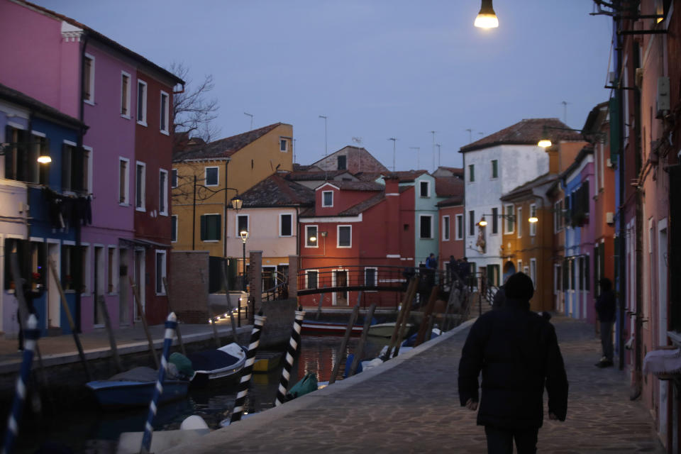 In this image taken on Thursday, Jan. 16, 2020, people walk at the Burano island, Italy. The Venetian island of Burano's legacy as a fishing village remains the source of its charms: the small colorful fishermen's cottages, traditional butter cookies that were the fishermen's sustenance at sea and delicate lace still stitched by women in their homes. As the island's population dwindles, echoing that of Venice itself, so too are the numbers of skilled artisans and tradespeople who have kept the traditions and economy alive. (AP Photo/Luca Bruno)