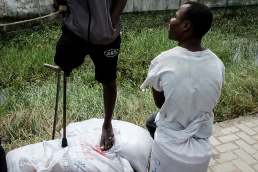 A man with one leg stands on sacks of rice printed 'China Aid,' looted from a warehouse in Beira