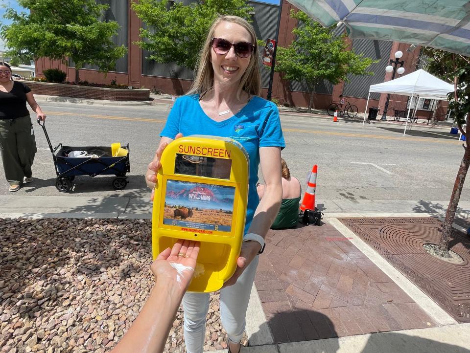 A smiling woman with sunglasses holding a yellow SPF dispenser as it dispenses sunblock onto the writer's hand