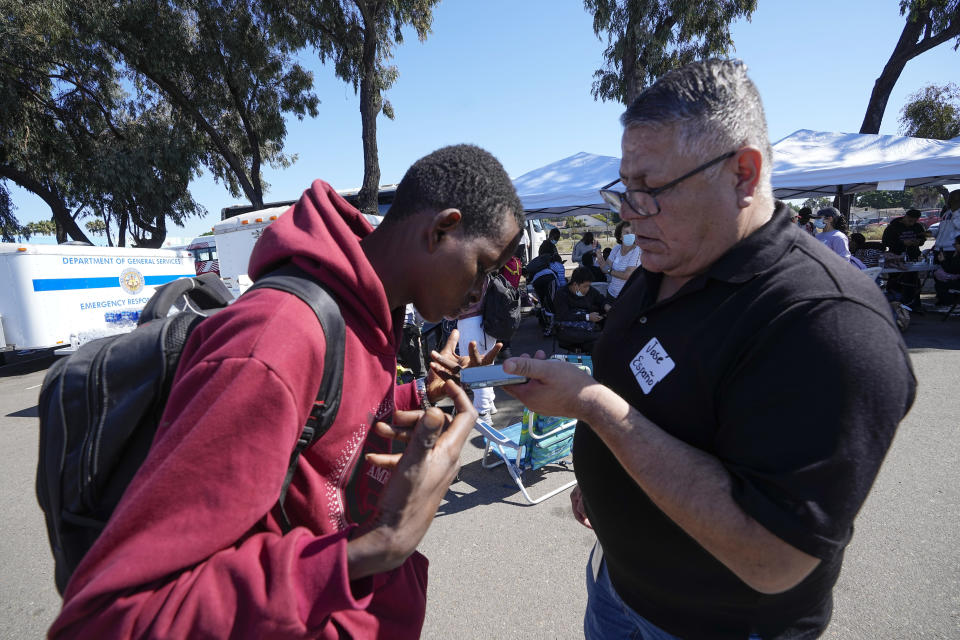 A volunteer, right, uses a translating app on his phone to speak with a migrant in French in a parking lot set up to help people with travel plans, accommodation, food and shelter, Friday, Oct. 6, 2023, in San Diego. San Diego's well-oiled system of migrant shelters is being tested like never before as U.S. Customs and Border Protection releases migrants to the streets of California's second-largest city because shelters are full. (AP Photo/Gregory Bull)