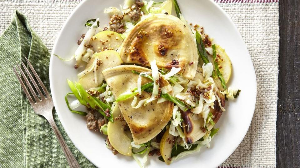 pierogies with sausage cabbage and pear on a white plate with a fork