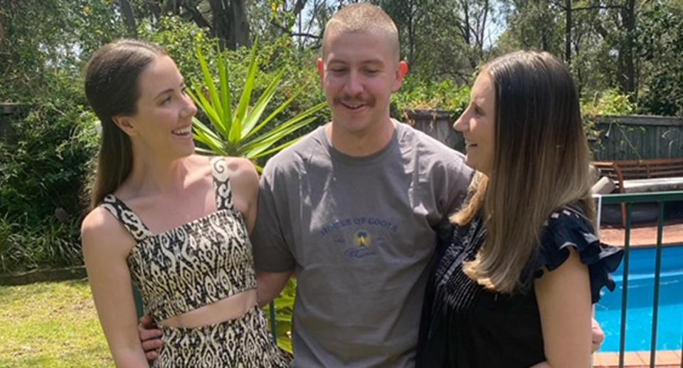 The three siblings are caught in a candid photo as they laugh while trying to pose for a picture in a backyard. 