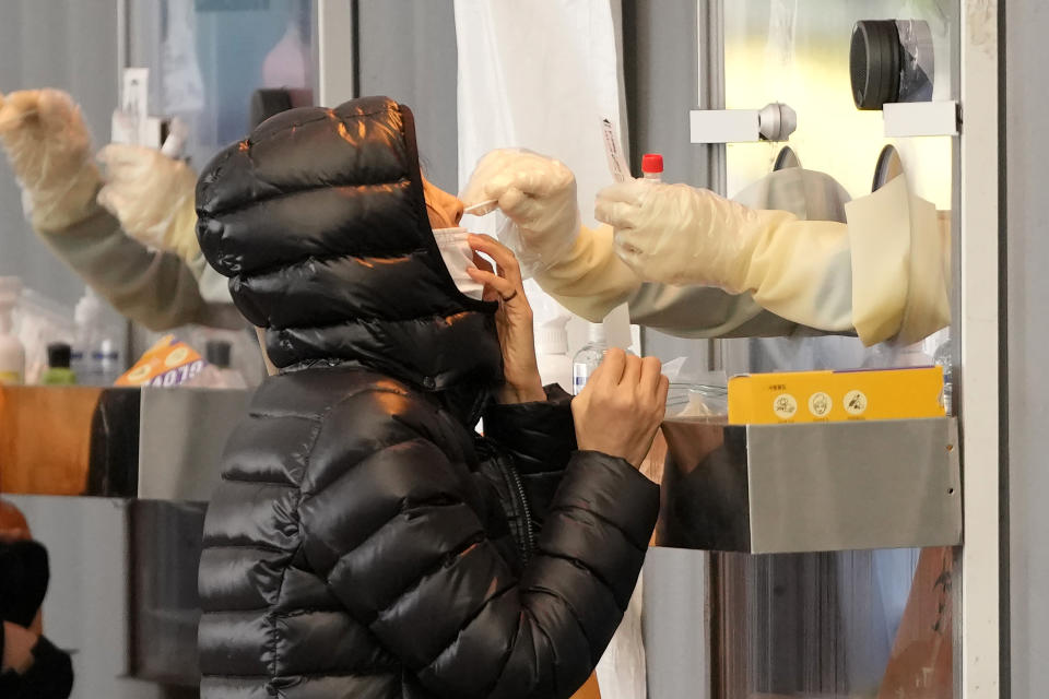 A medical worker wearing protective gear in a booth, takes sample from a woman at a temporary screening clinic for the coronavirus in Seoul, South Korea, Wednesday, Dec. 1, 2021. South Korea's daily jump in coronavirus infections exceeded 5,000 for the first time since the start of the pandemic, as a delta-driven surge also pushed hospitalizations and deaths to record highs. (AP Photo/Lee Jin-man)