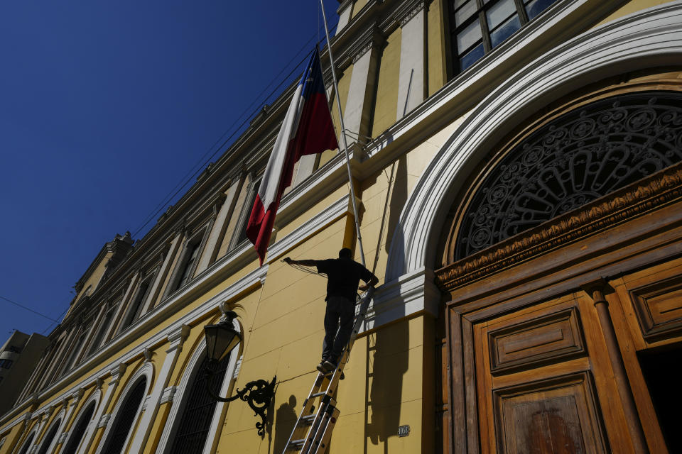 A University of Chile workers raises a national flag to fly at half-mast in mourning for three murdered police officers, in Santiago, Chile, Saturday, April 27, 2024. The police officers were killed early Saturday, in Cañete, Chile's Bío Bío region. (AP Photo/Esteban Felix)