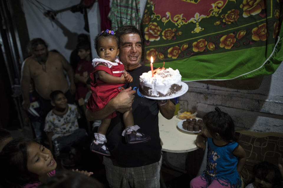 In this March 18, 2020 photo, Cesar Alegre carries his daughter Valerie while holding her store bought cake, as he and fellow residents prepare to mark her first birthday in the deteriorating building where they live, nicknamed “Luriganchito” after the country’s most populous prison, in Lima, Peru. Since the nationwide lockdown decreed by the government to curb the spread of the new coronavirus, Alegre and his children walk to a market every other day in hopes that merchants give them the overripe or expired food that nobody wants to buy. (AP Photo/Rodrigo Abd)