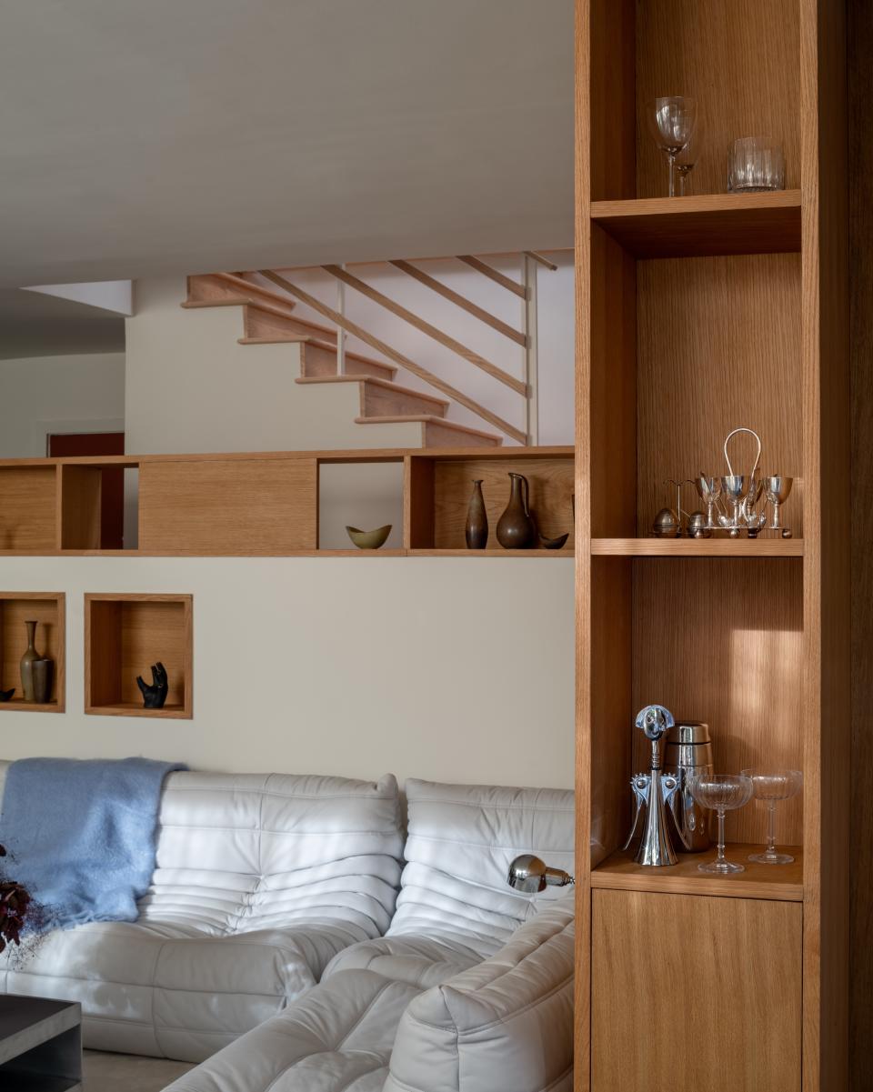 The millwork in the living room is full of peekaboo moments that reveal special objects sourced throughout the owners’ travels. Chief among them are a Carl Auböck Glove vase and a collection of vintage vessels by Gunnar Nylund. An open bar cabinet stands to the right.