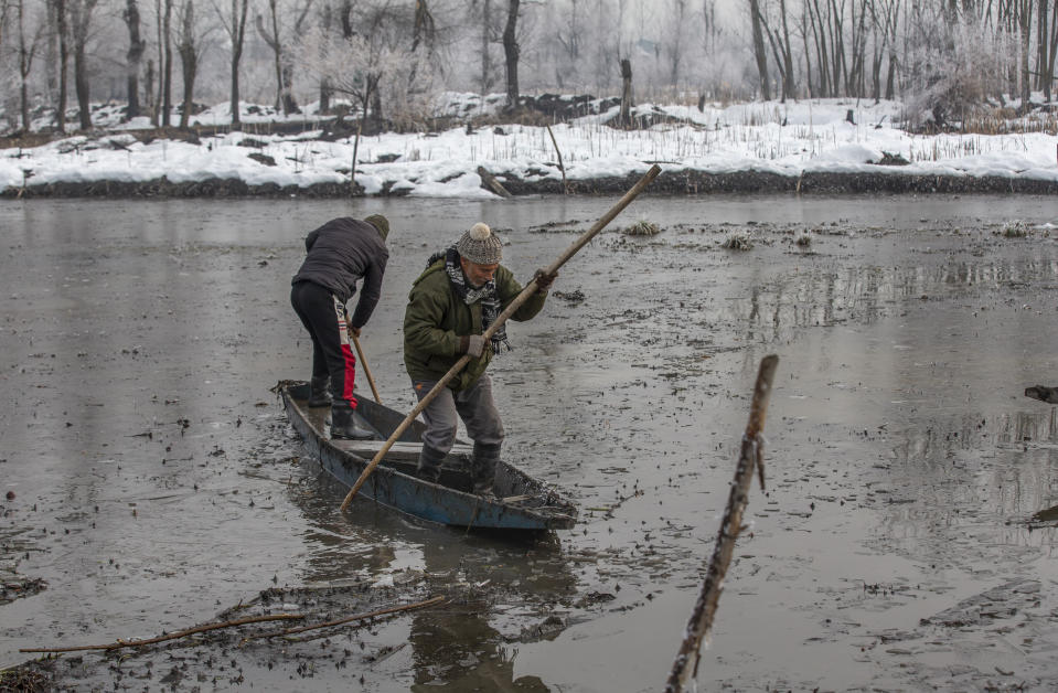 Wildlife officer Ghulam Mohiuddin Dar, right, along with a colleague Mushtaq Ahmad struggles to row their boat on the frozen surface of a wetland in Hokersar, north of Srinagar, Indian controlled Kashmir, Friday, Jan. 22, 2021. The officials have been feeding birds to prevent their starvation as weather conditions in the Himalayan region have deteriorated and hardships increased following two heavy spells of snowfall since December. Temperatures have plummeted up to minus 10-degree Celsius. (14 degrees Fahrenheit) (AP Photo/Dar Yasin)