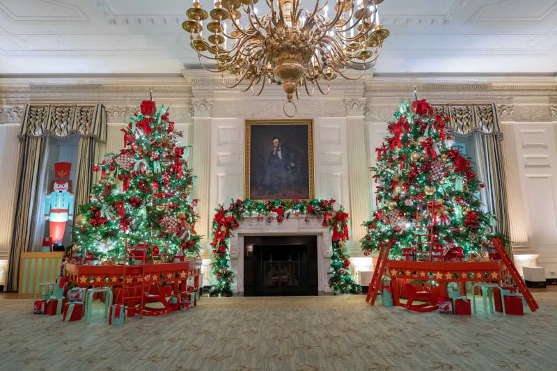 white fireplace with symmetrical Christmas trees in teal and red with large gold chandelier and presidential portrait