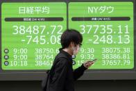 A person walks in front of an electronic stock board showing Japan's Nikkei and New York Dow indexes at a securities firm Tuesday, April 16, 2024, in Tokyo. (AP Photo/Eugene Hoshiko)