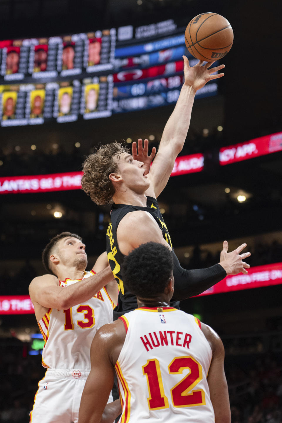 Utah Jazz forward Lauri Markkanen, top, scores between Atlanta Hawks guard Bogdan Bogdanovic (13) and forward De'Andre Hunter (12) during the first half of an NBA basketball game Tuesday, Feb. 27, 2024, in Atlanta. (AP Photo/Hakim Wright Sr.)