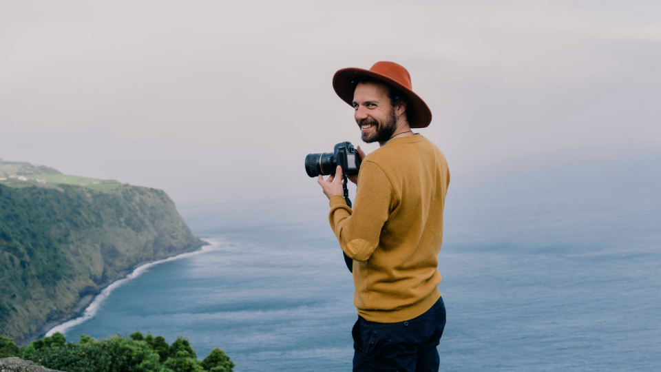 Pay for snaps: A man stands on the coast line of Portugal with a camera, smiling and looking back from the view.