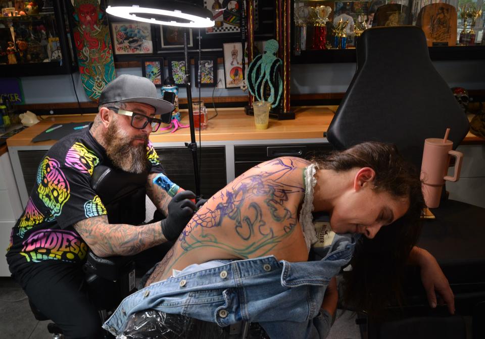 Mark Longenecker, owner of Endless Summer Tattoos in downtown Cocoa Beach, inks a traditional Japanese hanna mask on the back of Kristen Bahlke of Palm Bay. Mark has done a few other tattoos for her.