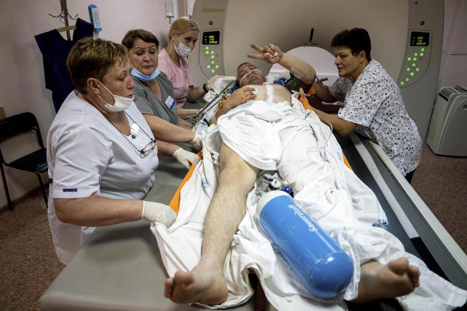 Medical workers move Mykola, a wounded Ukrainian serviceman, for CT scan while he shows a Victory sign at Mechnikov Hospital in Dnipro, Ukraine, Friday, July 14, 2023. A surge of wounded soldiers has coincided with the major counteroffensive Ukraine launched last month to try to recapture its land from Russian forces. Surgeons at Mechnikov Hospital, one of the country's biggest, are busier now than perhaps at any other time since Russia began its invasion 17 months ago. (AP Photo/Evgeniy Maloletka)