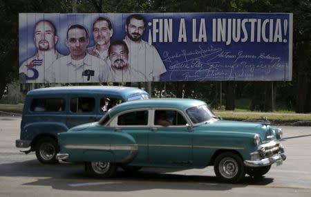 Cars drive past a banner featuring five Cuban prisoners held in U.S. custody, two of whom were previously released, in Havana December 17, 2014. REUTERS/Enrique De La Osa