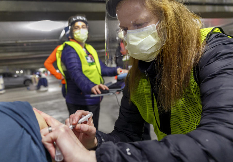 FILE - In this Jan. 10, 2021, file photo, pharmacist Colleen Naughtin, right, administers the Moderna COVID-19 vaccine at a drive-thru vaccination clinic in Portland, Ore. Questions about how a limited supply of vaccine should be distributed have found a new focus in rural America and from Oregon to Tennessee to upstate New York, complaints are surfacing in rural areas of a real — or perceived — inequity in vaccine allocation. (Kristyna Wentz-Graff/Pool Photo via AP, File)