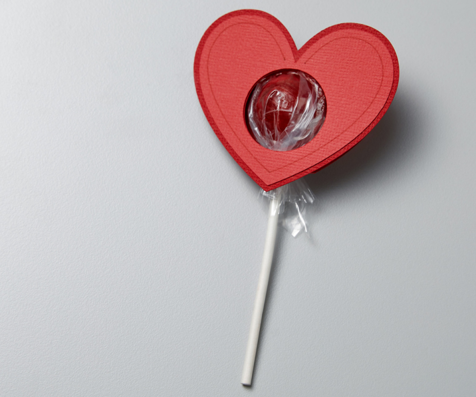 A cut out red love heart with a lollypop inserted.