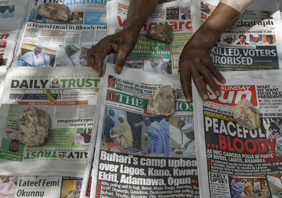 A newspaper vendor uses rocks to stop the day's front pages from blowing in the wind, at a newspaper stand in Kano, in northern Nigeria Sunday, Feb. 24, 2019. Vote counting continued Sunday as Nigerians awaited the outcome of a presidential poll seen as a tight race between the president and a former vice president. (AP Photo/Ben Curtis)