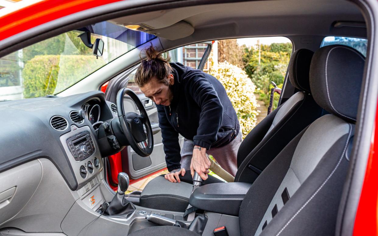 A young adult man cleaning out his car by vacuuming up the dirt and dust