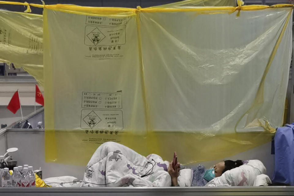 A resident rests using medical waste trash bags as a barrier at a temporary hospital converted from the National Exhibition and Convention Center to quarantine COVID-positive people in Shanghai, China on April 18, 2022. Interviews with family members of people testing positive for COVID-19, a phone call with a government health official and an independent tally raise questions about how Shanghai calculates virus cases and deaths, almost certainly resulting in a marked undercount. (Chinatopix via AP)