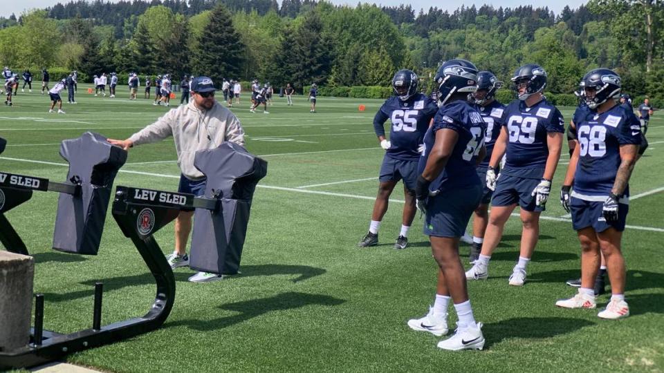 Offensive line coach Scott Huff (left, gray hoodie) instructs third-round NFL draft choice Christian Haynes (64) and fellow blockers on the first day of Seattle Seahawks rookie minicamp May 3, 2024, at the team’s Virginia Mason Athletic Center in Renton.