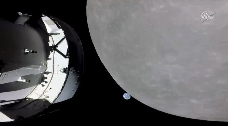 Esta captura de pantalla de NASA TV muestra la cápsula Orion de la NASA, a la izquierda, acercándose a la luna, a la derecha, el lunes 21 de noviembre de 2022. En el centro, la Tierra.