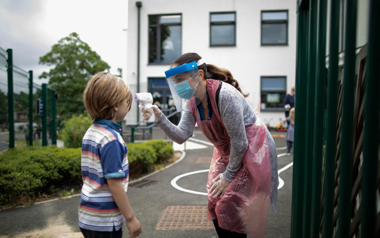 A teacher wearing personal protective equipment (PPE) takes a child's temperature - Getty Images/Getty Images Europe