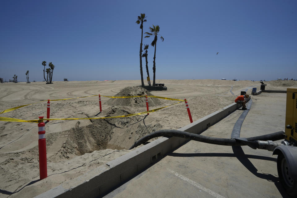 Seal Beach resident Tom Ostrom, right, sits along an empty water-pipe to be used to pump sea water back to the Pacific Ocean as homes are protected by sand berms in Seal Beach, Calif., Friday, Aug. 18, 2023. Hurricane Hilary is churning off Mexico's Pacific coast as a powerful Category 4 storm threatening to unleash torrential rains on the mudslide-prone border city of Tijuana before heading into Southern California as the first tropical storm there in 84 years. (AP Photo/Damian Dovarganes)