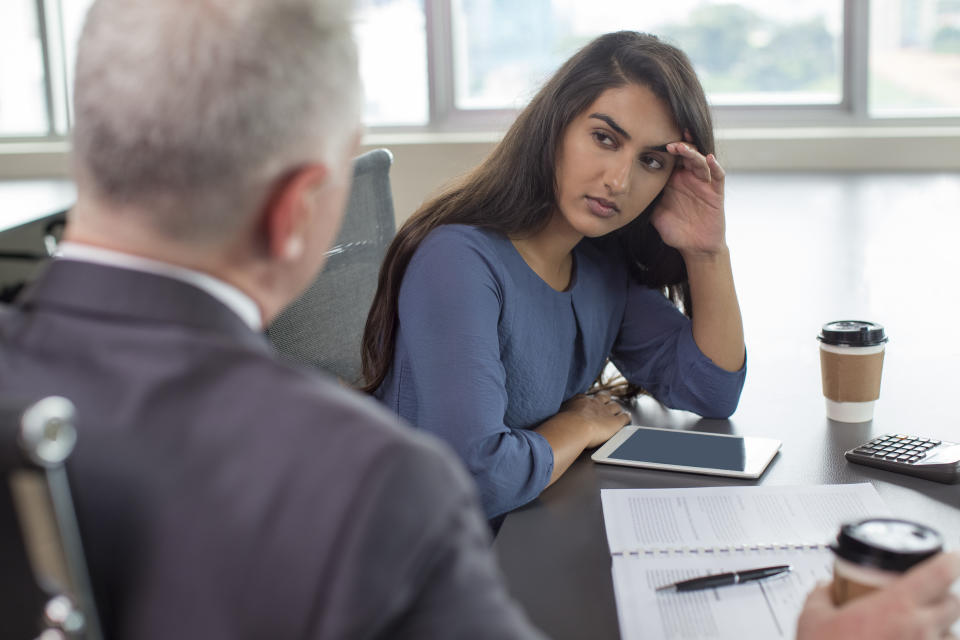 Business leader instructing focused Indian female assistant. Serious and upset woman leaning head on hand and listening to boss during coffee break. Teamwork or company hierarchy concept