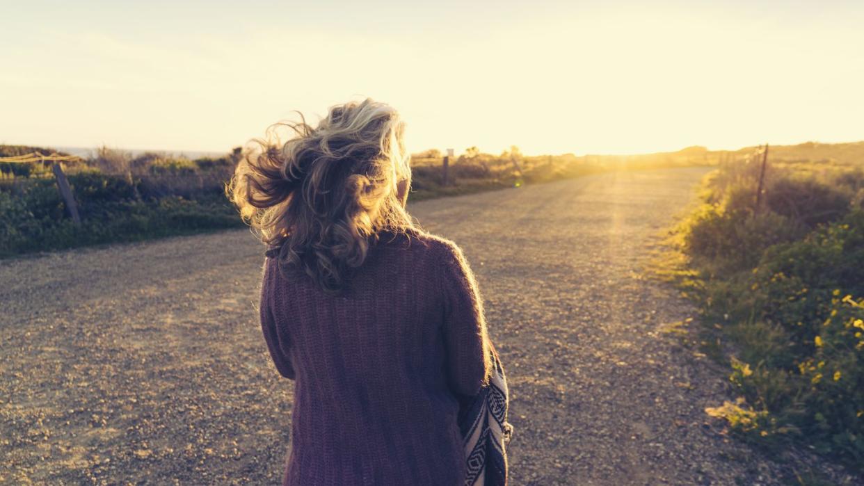 rear view of woman walking on dirt road during sunset