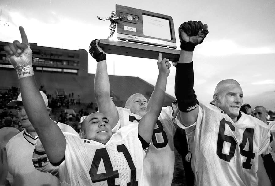 Brad Nading/Telegram Garden City High School’s Mike Sena, left, and Brandon Owston raise their arms in victory as Justin Wright holds the 6A footall trophy up to show the crowd Nov. 20, 1999 after winning the title over Olathe South, 14-7, at Wichita’s Cessna Stadium. (Courtesy: Finney County Historical Society)