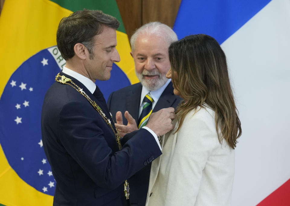 France's President Emmanuel Macron, left, presents Brazilian first lady Rosangela da Silva with the French honor, the Legion of Honor, as Brazilian President Luiz Inacio Lula da Silva looks on at Planalto presidential palace in Brasilia, Brazil, Thursday, March 28, 2024. (AP Photo/Eraldo Peres)