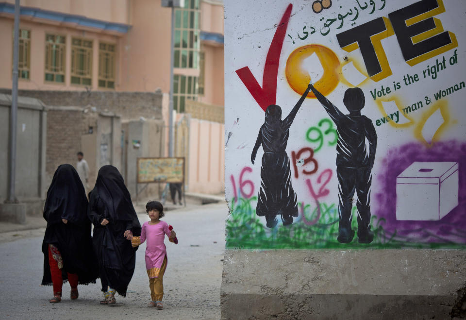 In this Wednesday, March 12, 2014 photo, two women in veils cross with a young girl a street next to an election poster demanding that voting is the right for every man and woman in Kandahar, southern Afghanistan. Still, many of the candidates or their running mates have violent histories. Several have been named by the U.S.-based Human Rights Watch as responsible for mass killings during the 1992 to 1996 civil war, fought between Islamic insurgents turned warlords who turned their guns on each other after throwing out the invading Soviet military. (AP Photo/Anja Niedringhaus)