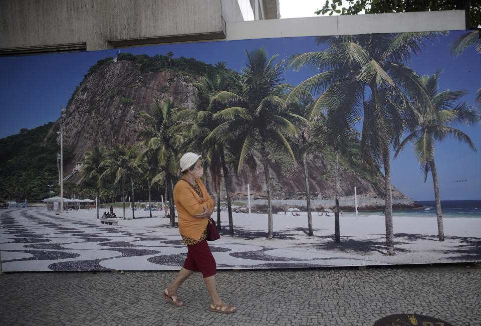 A woman walks past a landscape photo of Leme beach outside the closed Hilton hotel in Rio de Janeiro, Brazil, Wednesday, Aug. 26, 2020. Other hotel operators are offering hotel rooms for office space, aimed at enticing workers who need a home office without distractions, hoping to offset the sharp decline in tourist revenue due to the new coronavirus pandemic. (AP Photo/Silvia Izquierdo)