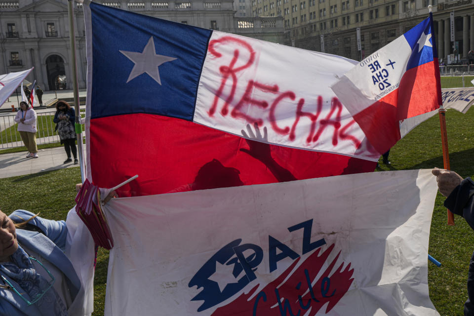 Personas con banderas se manifiestan en contra de la violencia y el nuevo proyecto de Constitución que será sometido a un plebiscito el 4 de septiembre, frente al palacio presidencial de La Moneda en Santiago, Chile, el viernes 12 de agosto de 2022. (Foto AP/Esteban Félix)