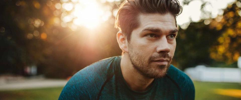 Close up portrait of healthy young man standing outdoors in park and looking away. Confident young man ready of workout.