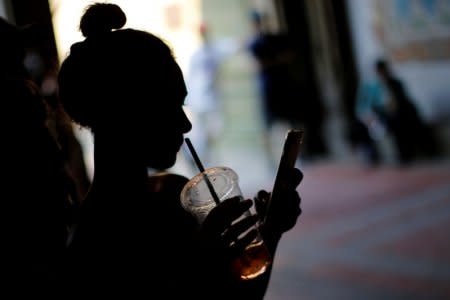 FILE PHOTO - A woman holds a drink while using her mobile phone on a hot summer day in Central Park, Manhattan, New York, U.S., July 01, 2018.  REUTERS/Eduardo Munoz