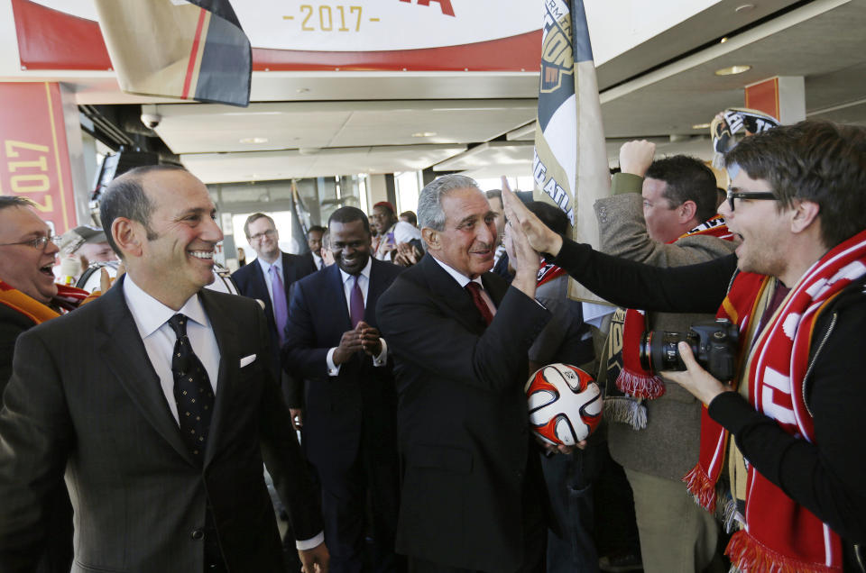 Atlanta Falcons owner Arthur Blank, center right, high-fives a fan upon arriving for a news conference with Major League Soccer Commissioner Don Garber, left, and Atlanta Mayor Kasim Reed, rear, to announce the city will be getting an MLS expansion team, Wednesday, April 16, 2014, in Atlanta. MLS announced its newest franchise, which will begin play in 2017 at the city's new retractable-roof stadium. The team will be owned by Blank. He donned a traditional soccer scarf and was serenaded by a burgeoning fan group that calls itself "Terminus Legion," a reference to the city's former name. (AP Photo/David Goldman)