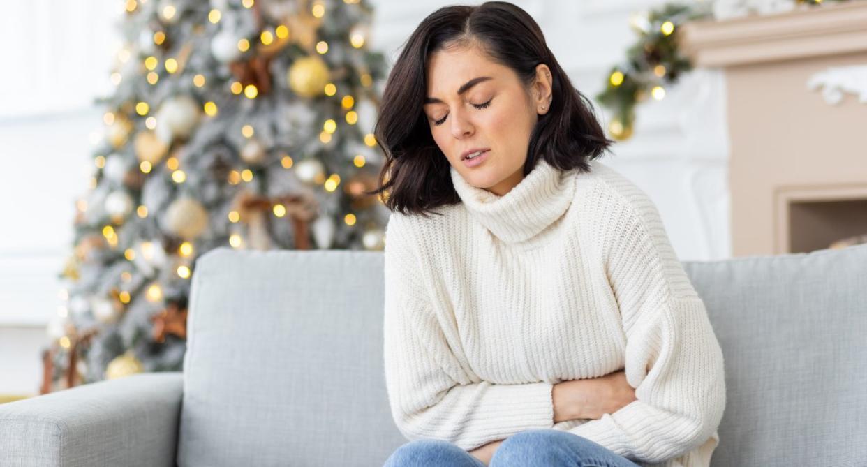 Woman with Christmas digestive issues, holding hurting stomach on sofa. (Getty Images)