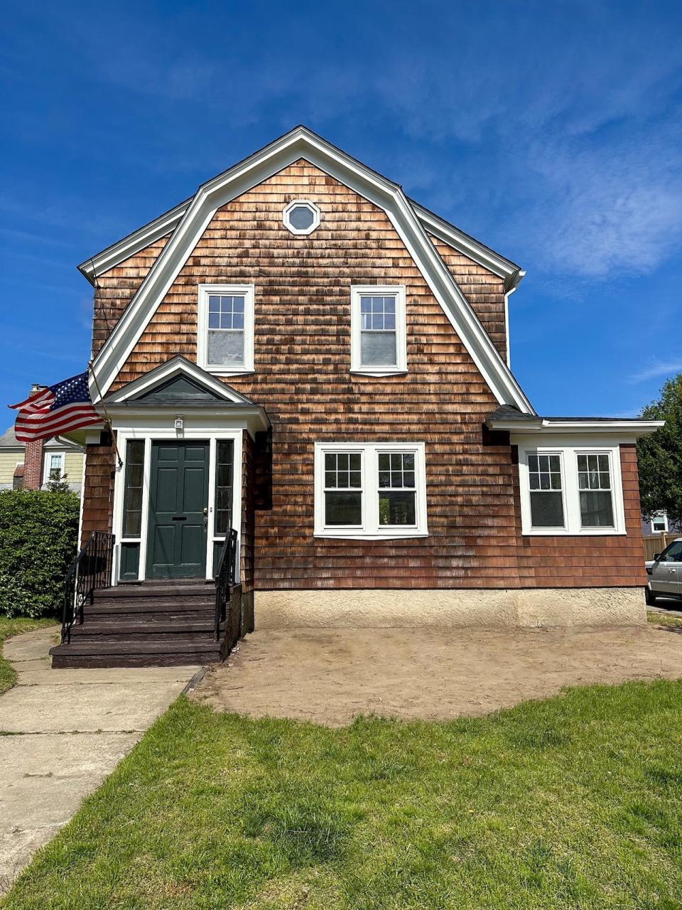 An exterior shot of a cottage in Rhode Island that has brown wooden paneling, white windows, and a dark green front door.