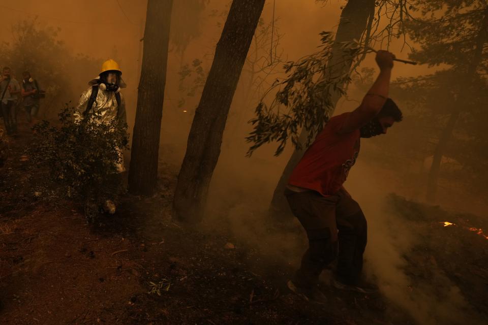 People try to extinguish the flames during a wildfire at Pefki village on Evia island, about 189 kilometers (118 miles) north of Athens, Greece, Sunday, Aug. 8, 2021. Pillars of billowing smoke and ash are blocking out the sun above Greece's second-largest island as a days-old wildfire devours pristine forests and triggers more evacuation alerts. (AP Photo/Petros Karadjias)