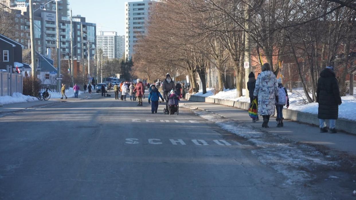 Adults and children walk along Alice Street near école élémentaire publique Trille des Bois in Ottawa's Vanier community on Feb. 6, 2024, the first day of a pilot project closing the street for part of the morning. (Nelly Albérola/Radio-Canada - image credit)