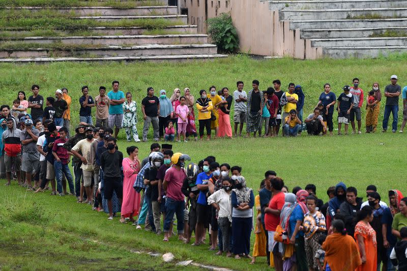 People stand in line for aid assistance at the Manakarra stadium following an earthquake in Mamuju