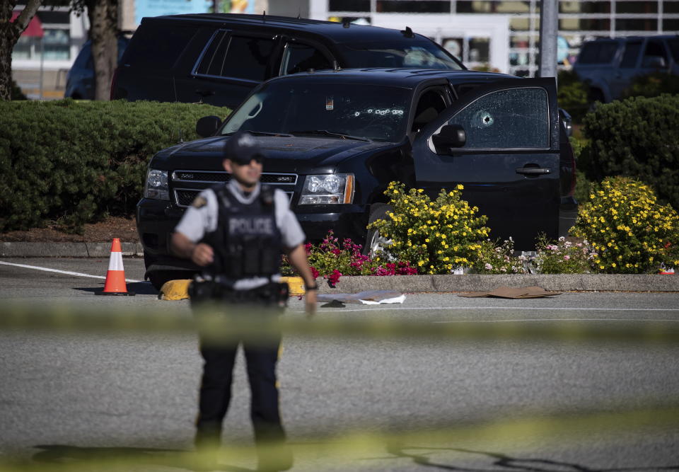 A police officer stands near a RCMP vehicle with bullet holes in the windshield and driver's side window at the scene of a shooting in Langley, British Columbia, Monday, July 25, 2022. (Darryl Dyck/The Canadian Press via AP)
