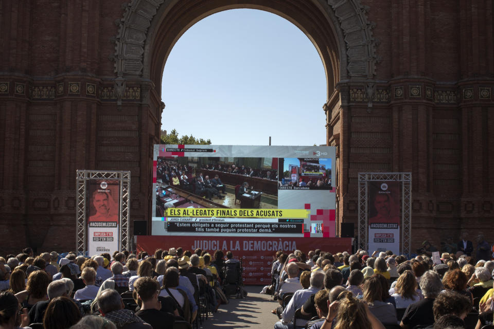 People look at Jordi Cuixart, leader of Omnium Cultural speaking on a big TV screen, during the trial at Spain's Supreme Court in Madrid on Wednesday, June 12, 2019, as they gather in downtown Barcelona, Spain. A dozen politicians and activists on trial for their failed bid in 2017 to carve out an independent Catalan republic in northeastern Spain will deliver their final statements Wednesday as four months of hearings draw to an end. (AP Photo/Emilio Morenatti)
