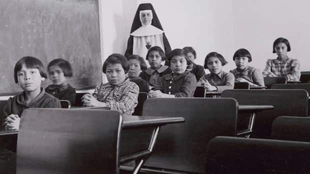 Students and a nun pose in a classroom at Cross Lake Indian Residential School in Cross Lake, Man., in February 1940. Canada's Catholic bishops have pledged $30 million to help survivors of residential schools. (Library and Archives Canada - image credit)
