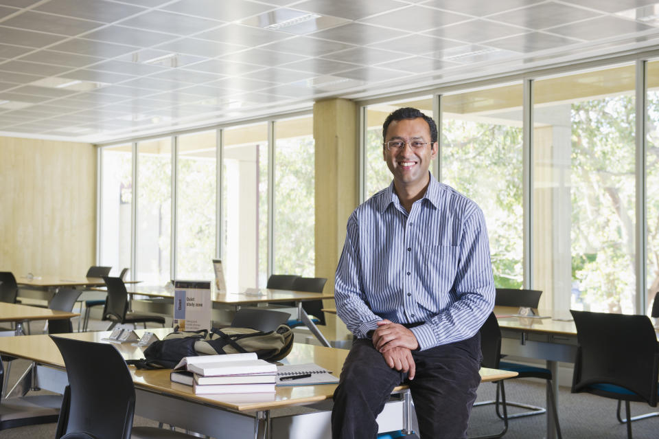 Indian teacher leaning on desk in classroom