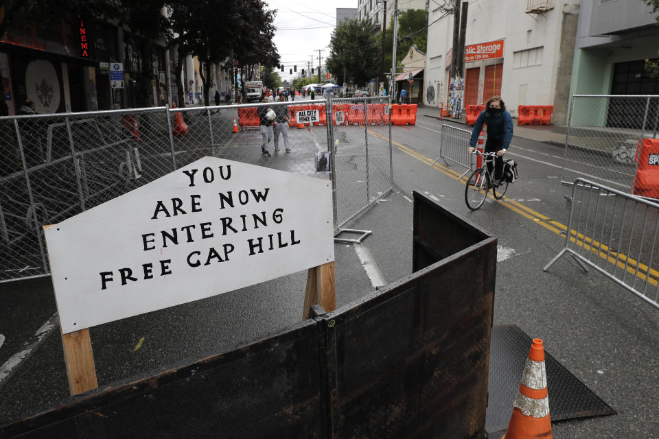 A cyclist rides near a sign that reads "You are now entering free Cap Hill," Thursday, June 11, 2020, inside what is being called the "Capitol Hill Autonomous Zone" in Seattle. Following days of violent confrontations with protesters, police in Seattle have largely withdrawn from the neighborhood, and protesters have created a festival-like scene that has President Donald Trump fuming. (AP Photo/Ted S. Warren)