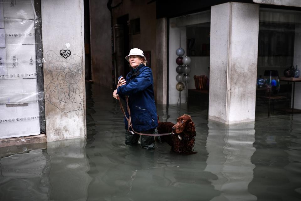 A woman walks her dog through a flooded street after an exceptional overnight "Alta Acqua" high tide water level, on November 13, 2019 in Venice. - Powerful rainstorms hit Italy on November 12, with the worst affected areas in the south and Venice, where there was widespread flooding. Within a cyclone that threatens the country, exceptional high water were rising in Venice, with the sirocco winds blowing northwards from the Adriatic sea against the lagoons outlets and preventing the water from flowing back into the sea. At 22:40pm the tide reached 183 cm, the second measure in history after the 198 cm of the 1966 flood. (Photo by Marco Bertorello / AFP) (Photo by MARCO BERTORELLO/AFP via Getty Images)